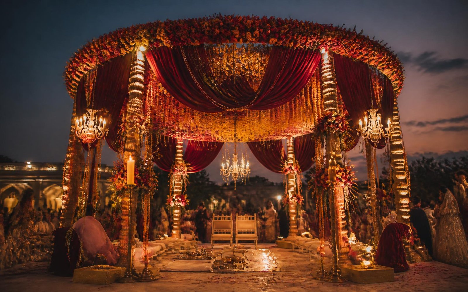 Mandap decorated with maroon drapes, marigolds and warm lighting at dusk